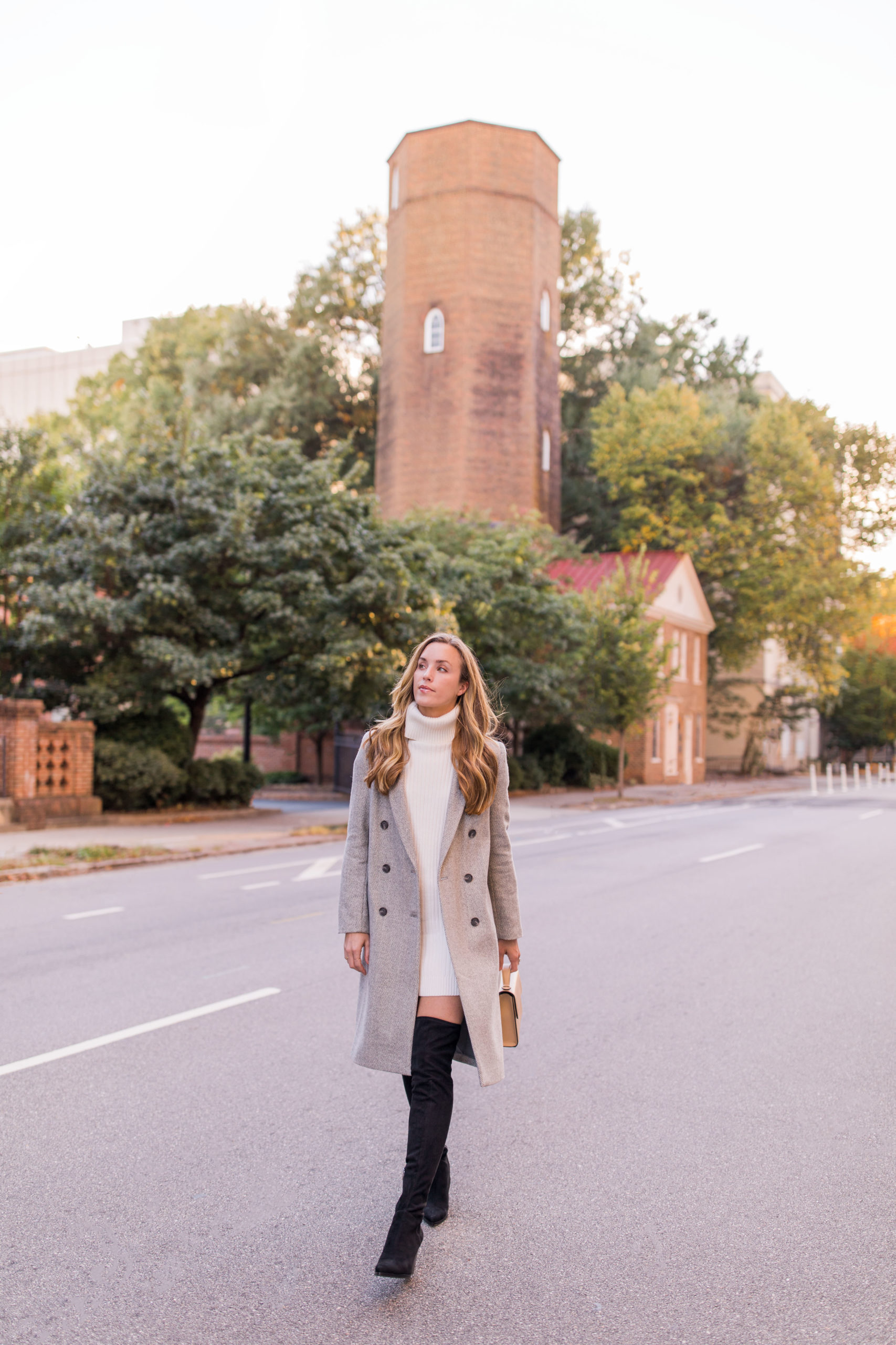 woman wearing sweater dress outfit with long wool coat, white turtleneck sweater dress, and over the knee boots