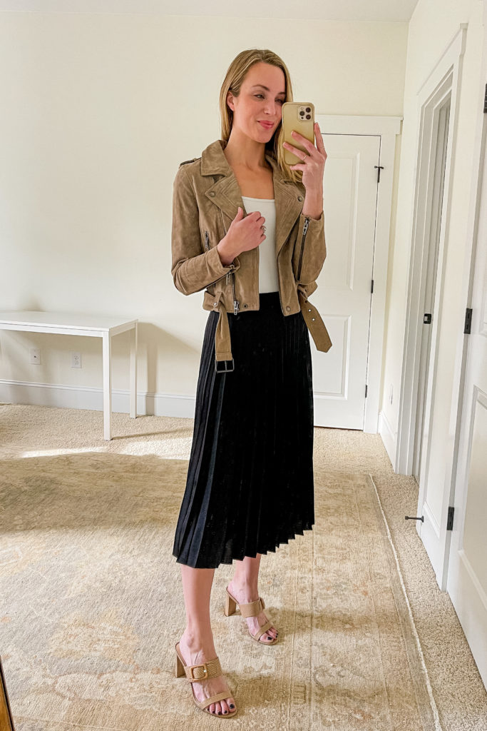 woman wearing pleated midi skirt with white bodysuit, moto jacket, and heeled sandals
