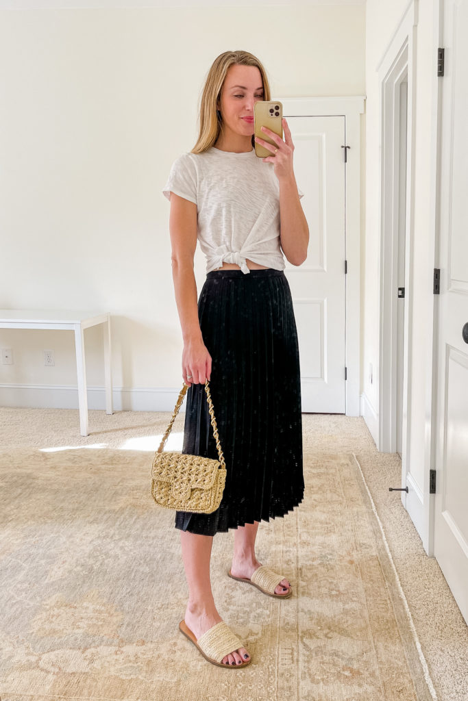 woman wearing black pleated midi skirt outfit with woven sandals, woven bag, and white tshirt