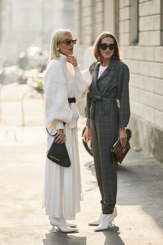 two women in street style photograph wearing white oversized sweater with white pleated skirt and white boots
