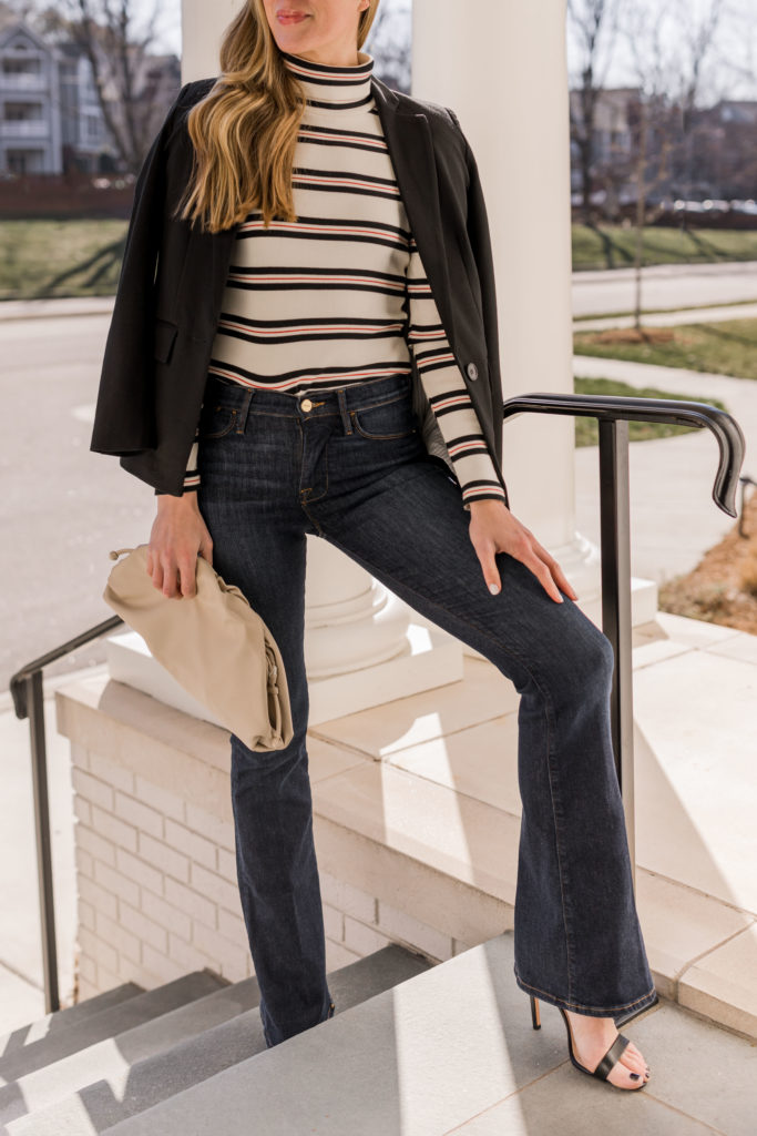 woman wearing black single breasted blazer striped valentines day turtleneck frame flare jeans and cream pouch clutch