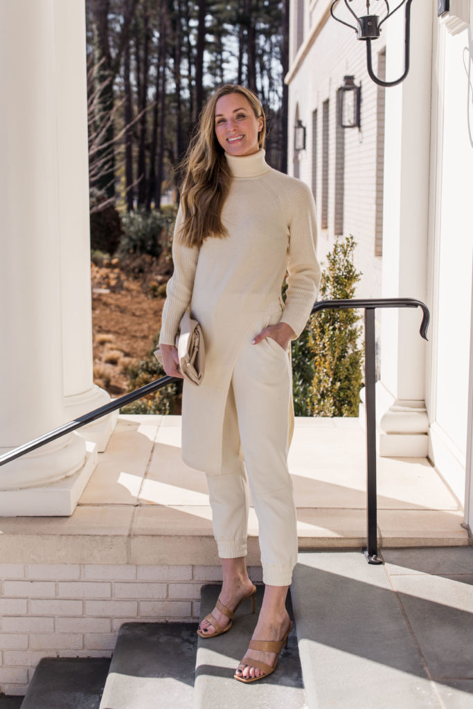 woman wearing all white turtleneck outfit with long side slit turtleneck white joggers and heeled sandals
